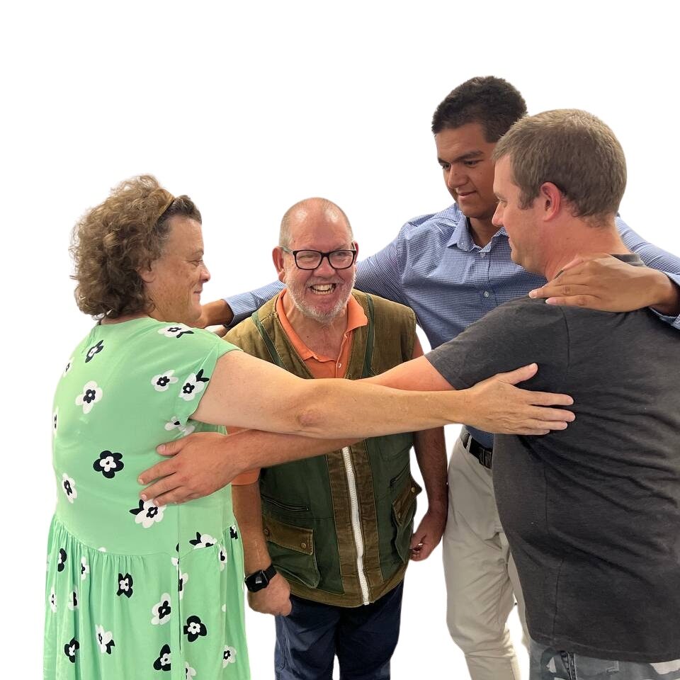 3 people in a circle with their arms on each others shoulders protecting a person standing in the middle in a group hug